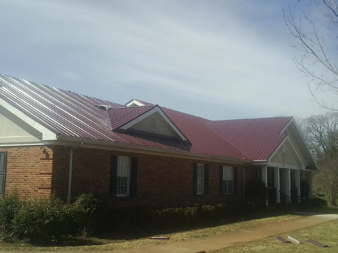 Red metal roof with gabled entries on a long brick building, from a Hail Damage Roof Repair job in Guerneville