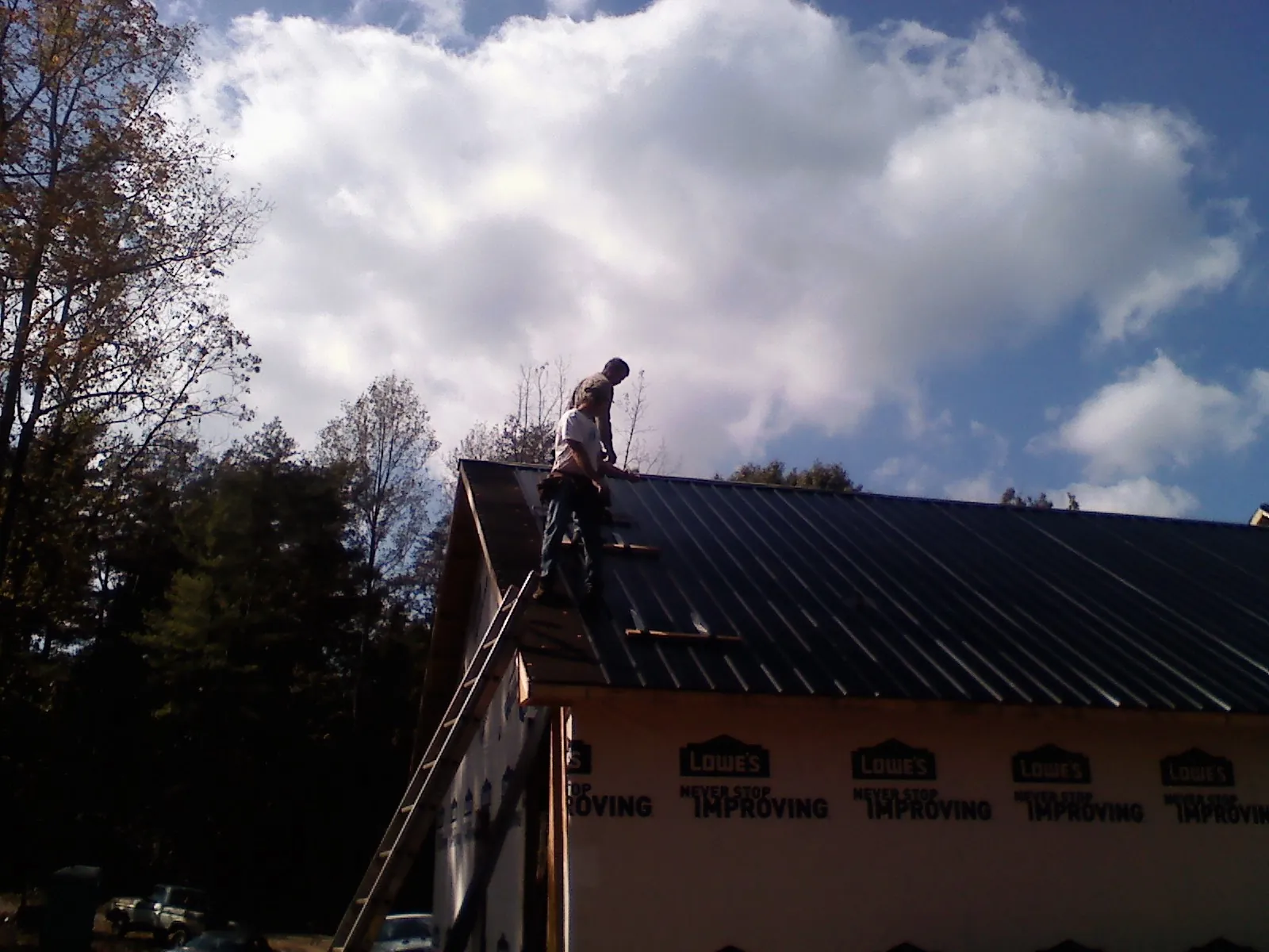 Roofer fastening dark metal panels high against a cloudy sky, from a Roof Inspection job in Guerneville
