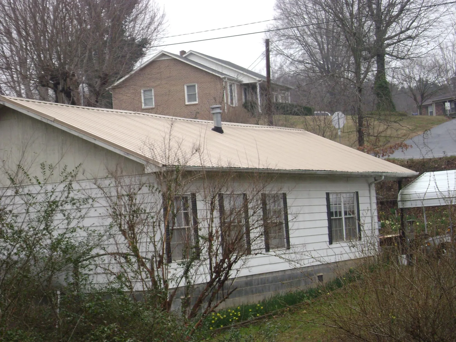 Tan metal roof on a white sided house set into a hillside — Commercial Roofing by Roofing Brothers in Guerneville
